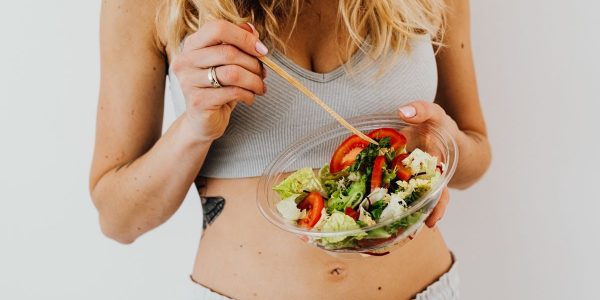 Woman in sports attire enjoys a fresh, nutritious salad, embodying a healthy lifestyle.