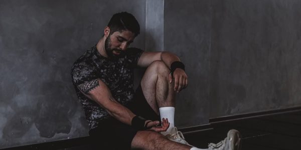 A muscular man in a gym environment taking a moment of rest, reflecting in a dark moody setting.